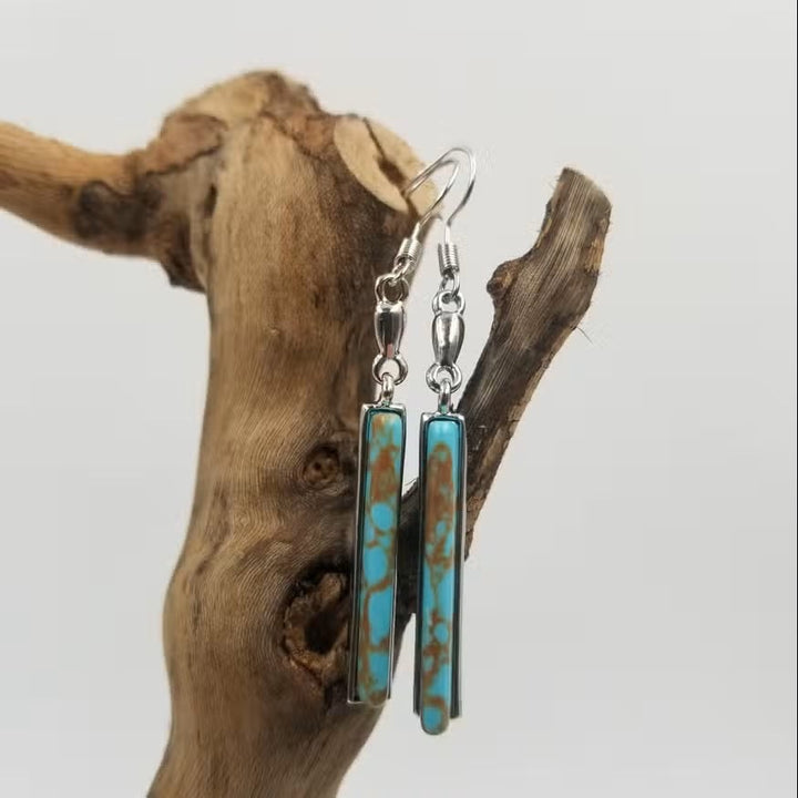 Close-up of vintage turquoise drop earrings with intricate detailing on a neutral background