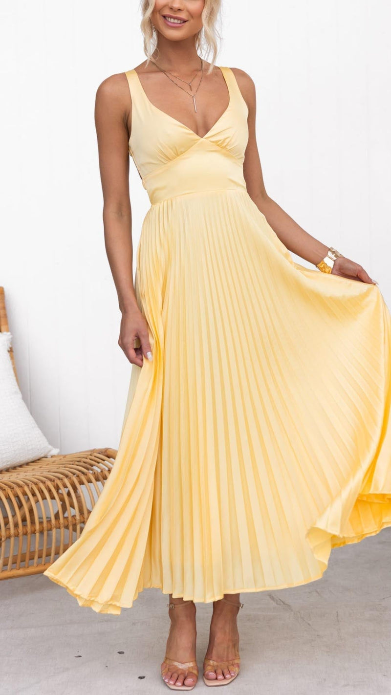 Woman wearing a yellow pleated V-neck maxi dress with a cinched waist and adjustable crisscross back straps