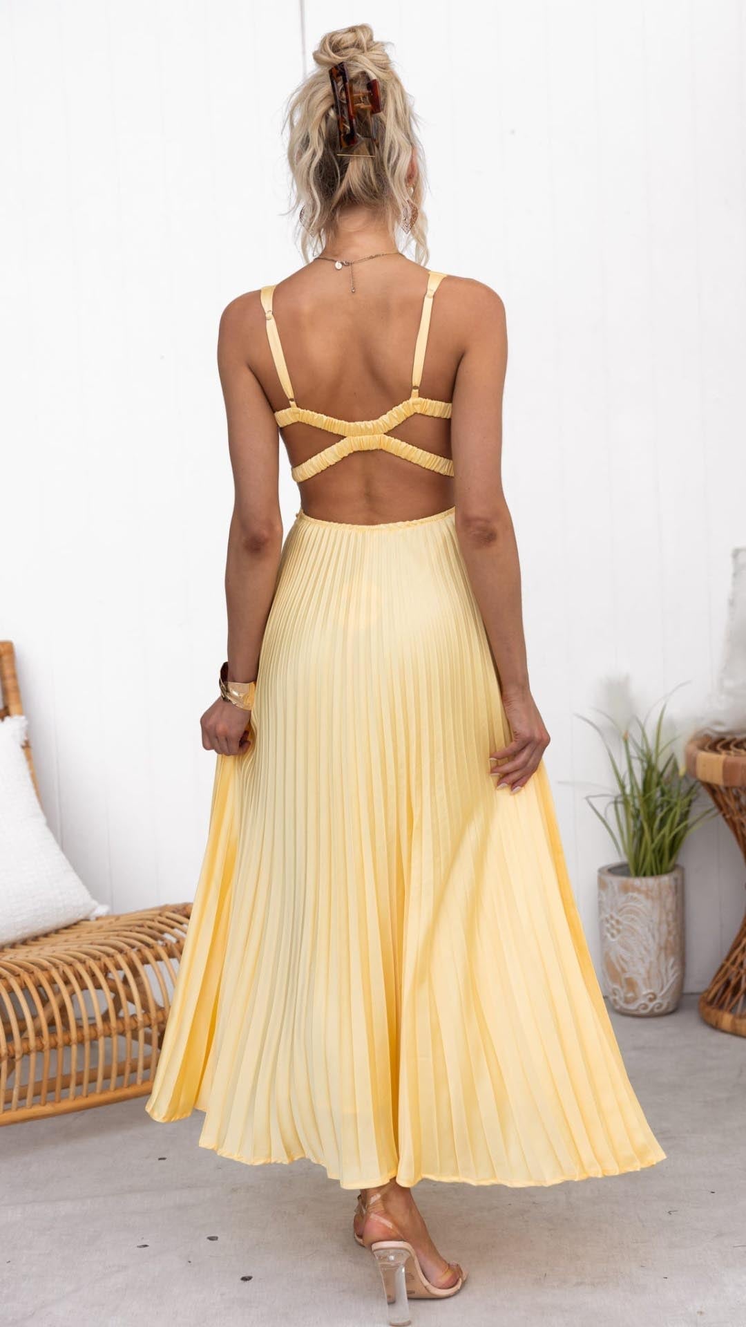 Full-length side view of woman in yellow pleated V-neck maxi dress