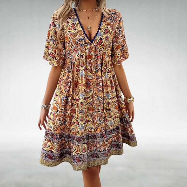 Woman wearing the Laurel paisley boho mini dress in green, standing in a sunny outdoor setting