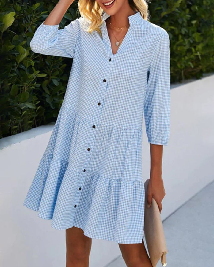Woman wearing a blue check summer dress with a tiered skirt and front button detail, styled for a casual daytime look