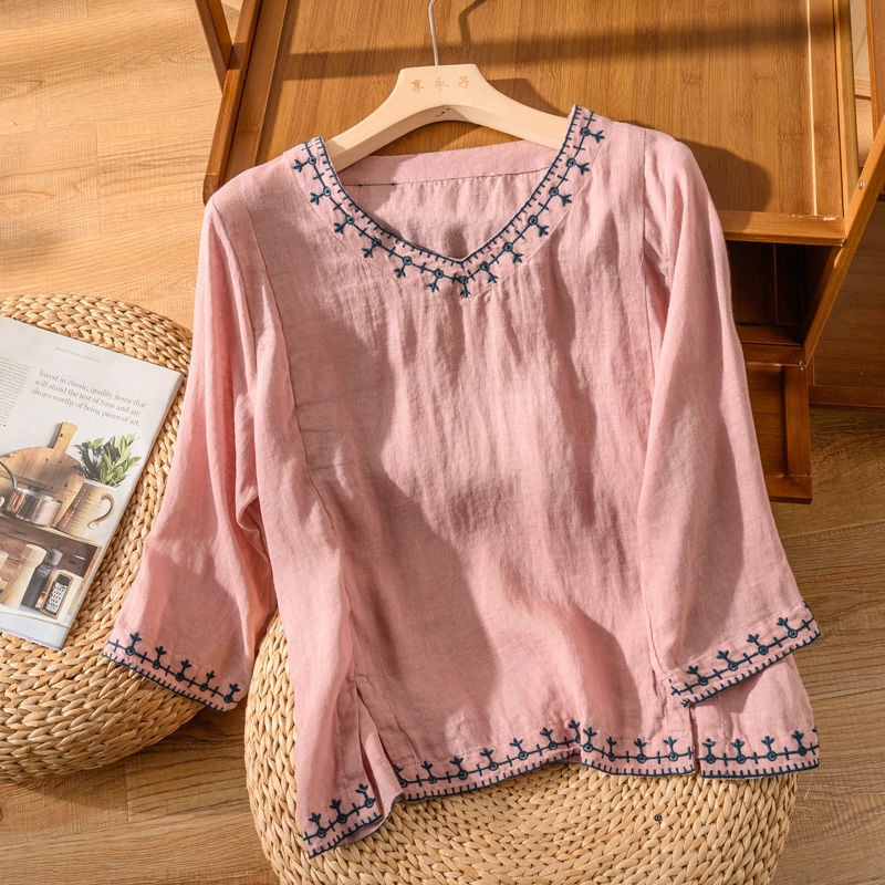 Close-up of embroidered hem and neckline detail on a lightweight V-neck blouse in white