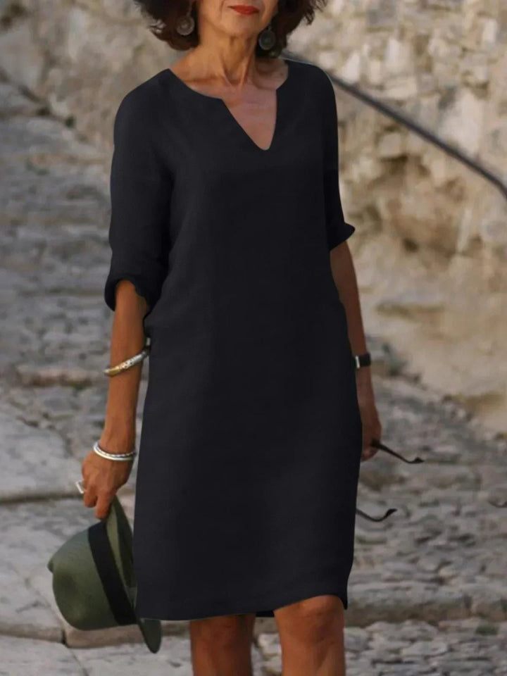Woman wearing a black elegant V-neck dress with pleated details and flattering belly coverage